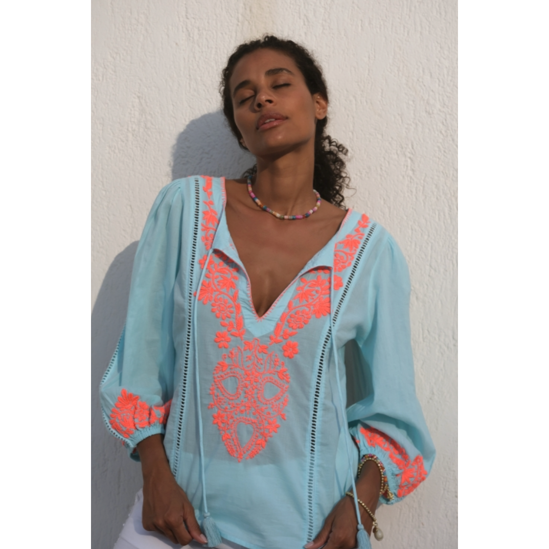 Made with classic cotton and featuring a stylish balloon sleeve, this top is elevated with neon pink embroidery on the front, back, and cuffs. The blanket stitch on the neck and tie tassels add a unique touch. Stay cool and chic this season.